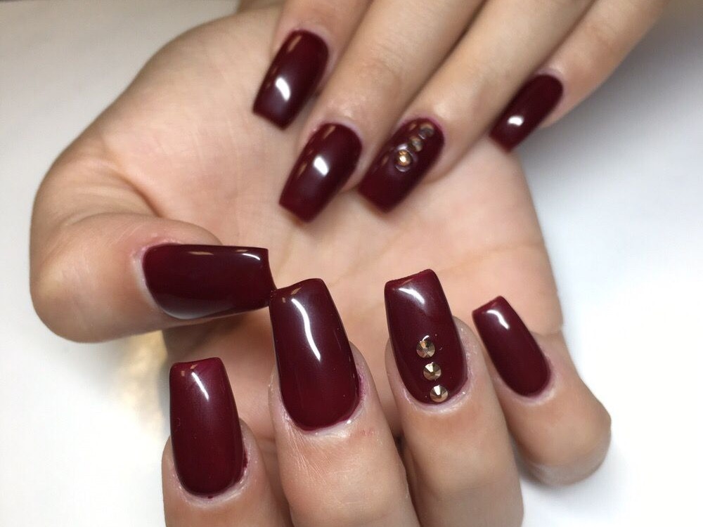 Square nails in glossy burgundy with small gold studs on two nails