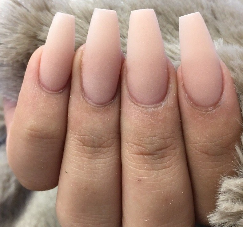 Long coffin nails in matte nude pink, fingers resting on beige faux fur